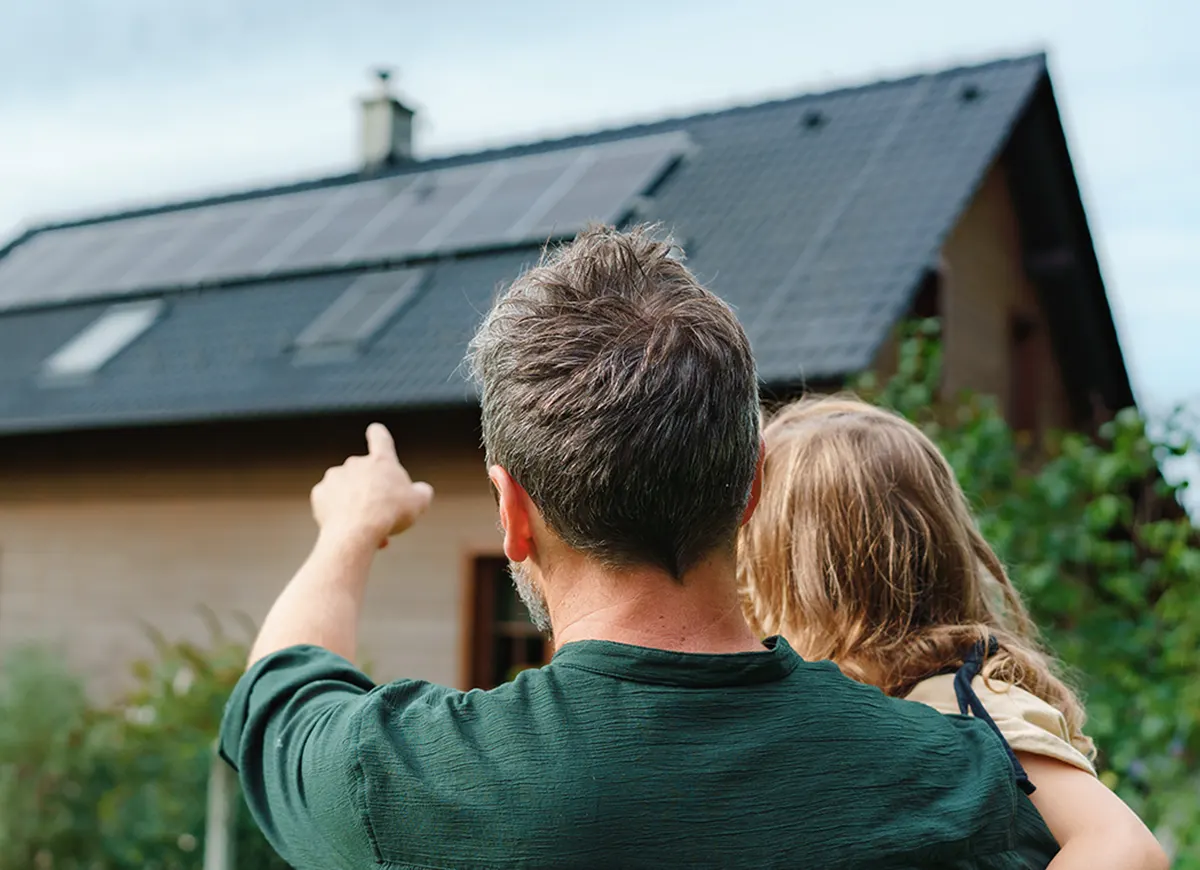 Un papa pointe des panneaux solaires avec son enfant dans les bras